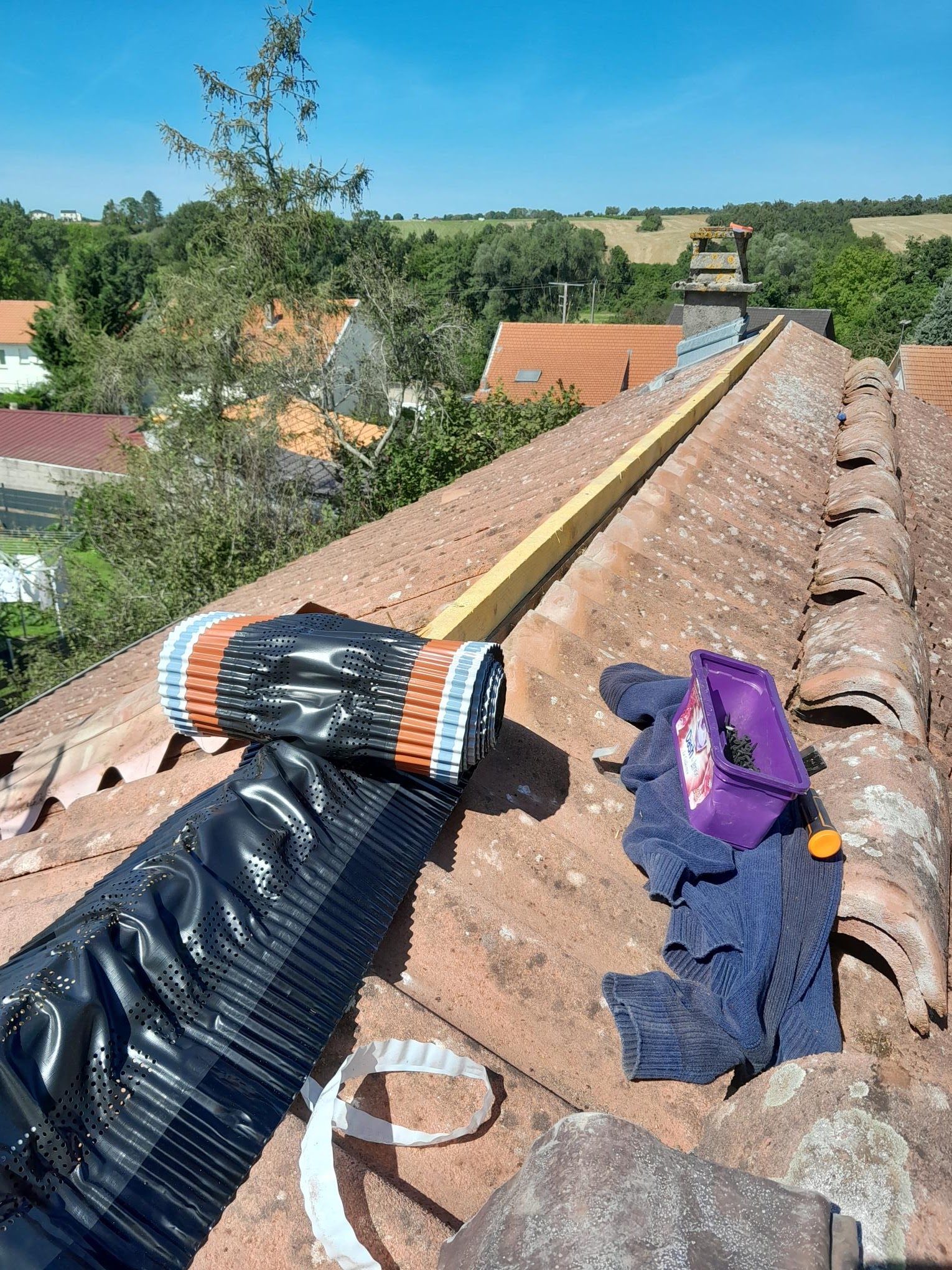 Travaux de faîtage sur une toiture en tuiles, rouleau de closoir posé sur le toit